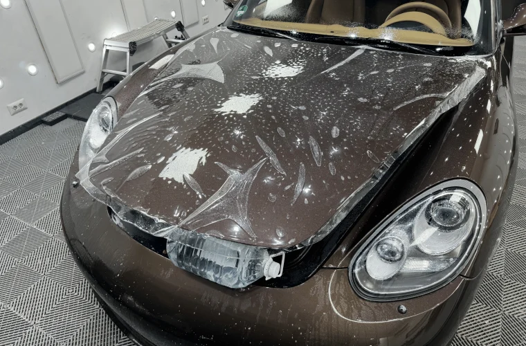 Folie PPF așezată pe capota unui Porsche Boxster maro, în timpul aplicării cu soluție de montaj