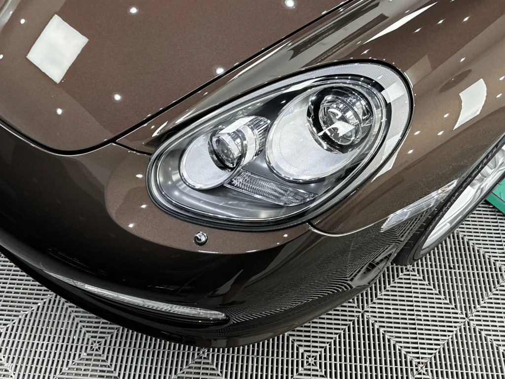 Farul și colțul barei față ale unui Porsche Boxster maro, după aplicarea foliei PPF