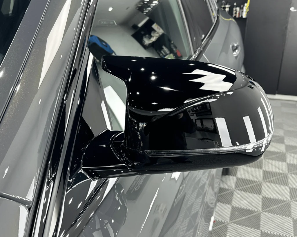 Carcasa neagră lucioasă a oglinzii unui BMW X6M după aplicarea foliei PPF