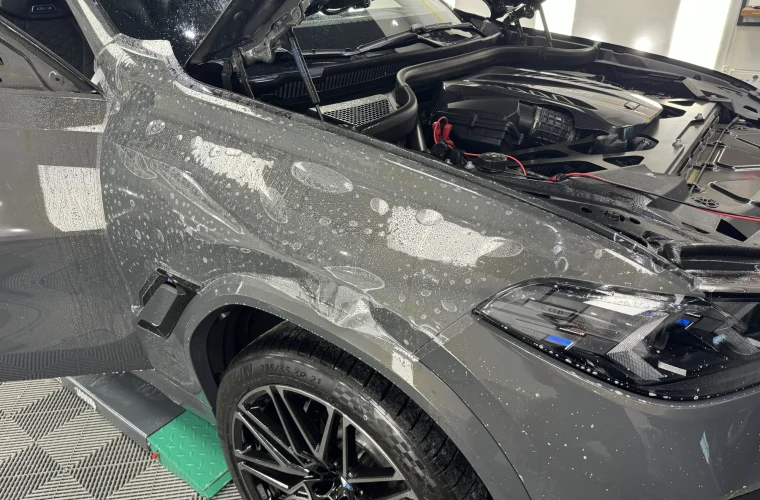 Folie PPF aplicată umed pe aripa față a unui BMW X6M, cu capota ridicată